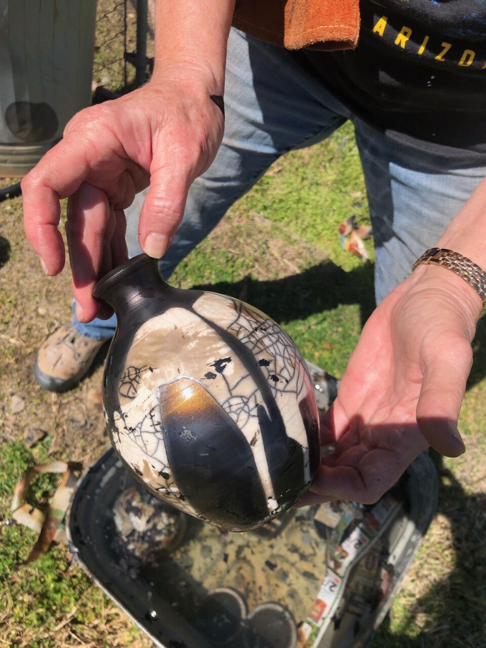 Judi Harwood holding finished raku pot pulled out of water, crackle glaze