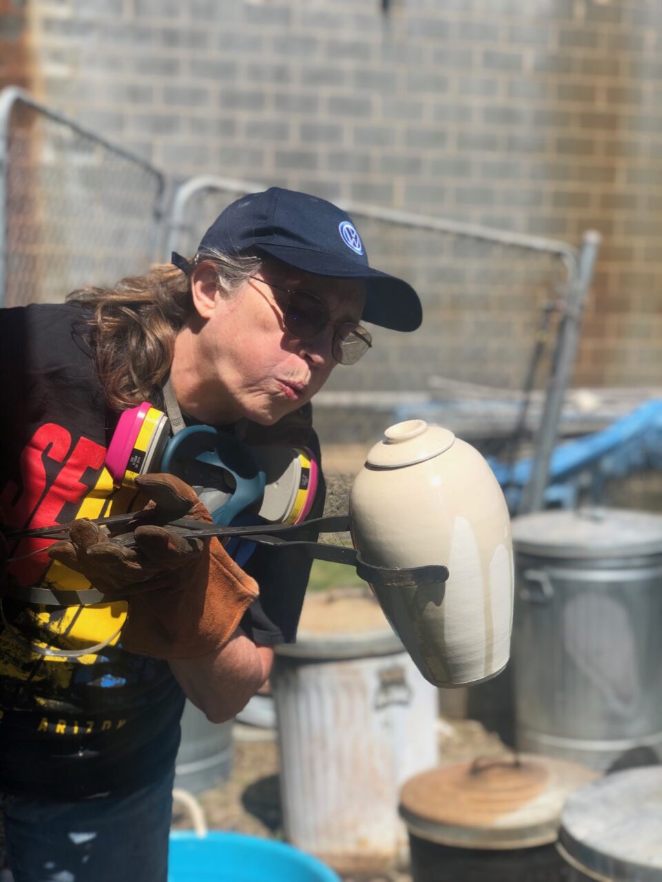 Judi Harwood holding hot raku pot with tongs, blowing on crackle glaze