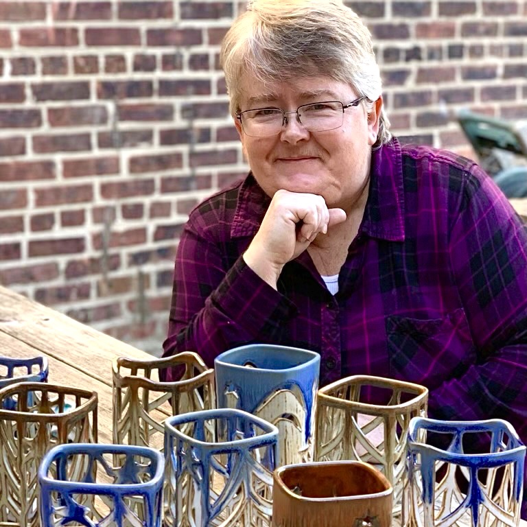 Julia Mann sitting, smiling with finished pots, pierced lanterns