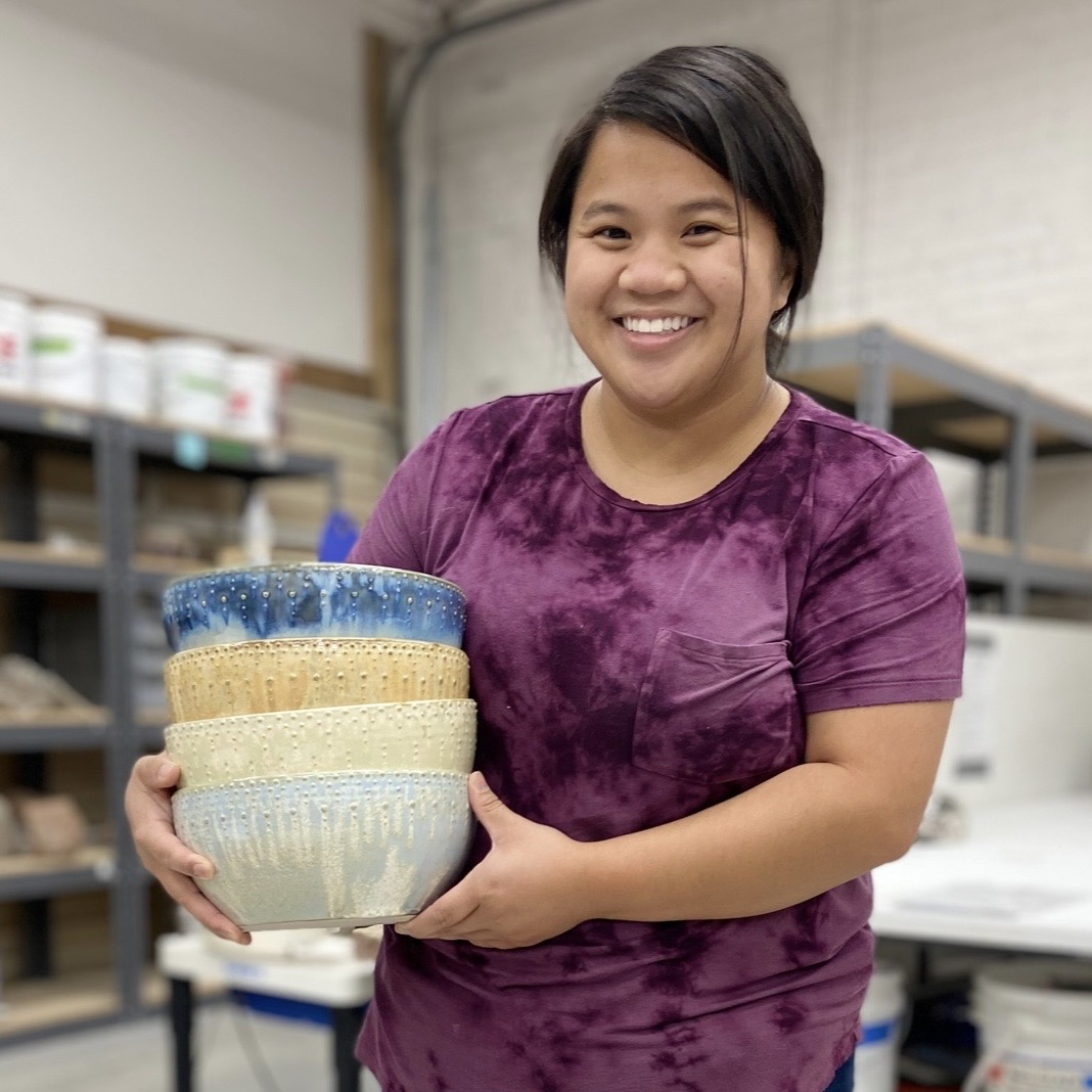 Katie Meili Messersmith holding stack of dotted serving bowls in ISM studio, dot pots