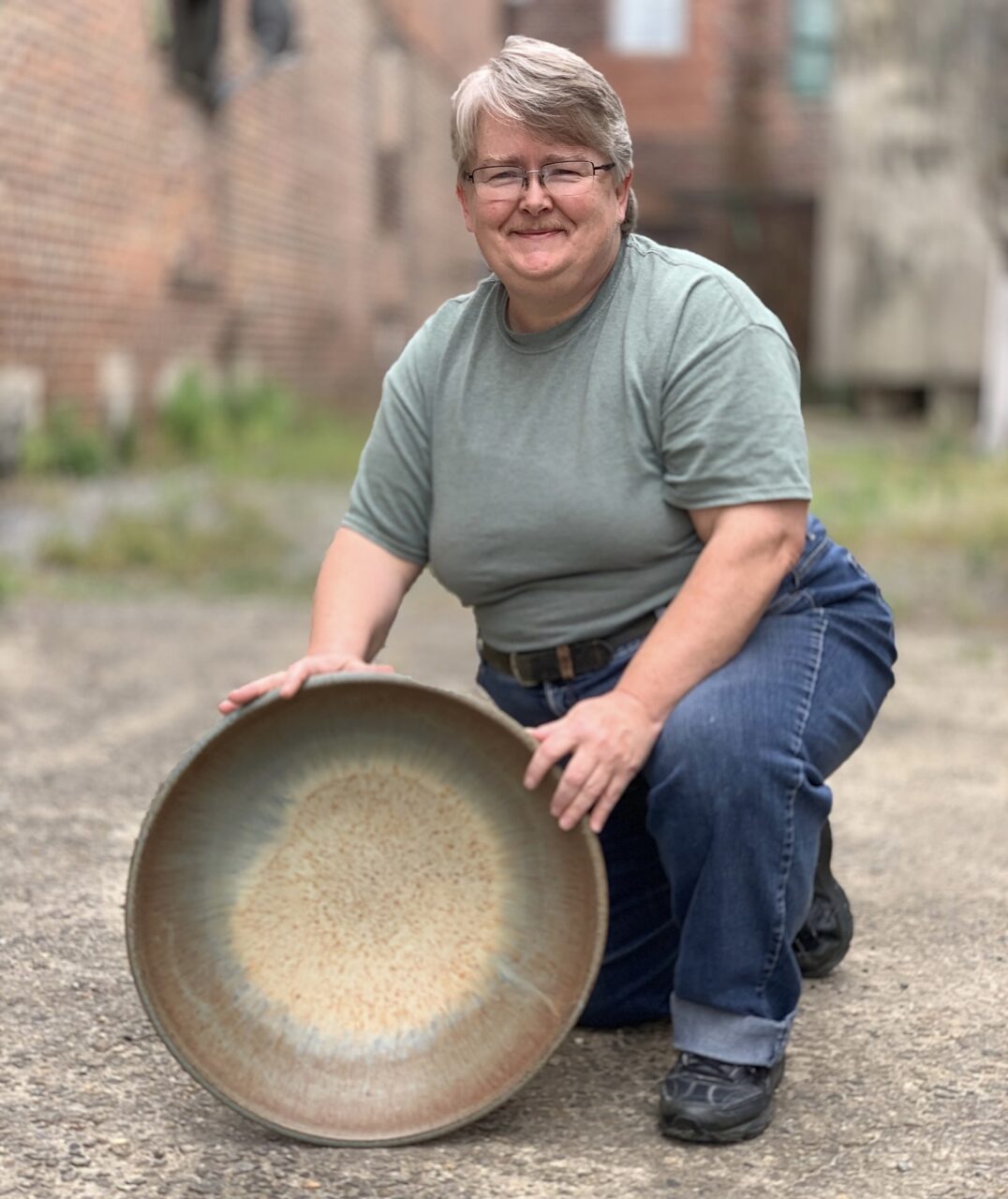 Julia Mann kneeling with her finished pot, large bowl, smiling