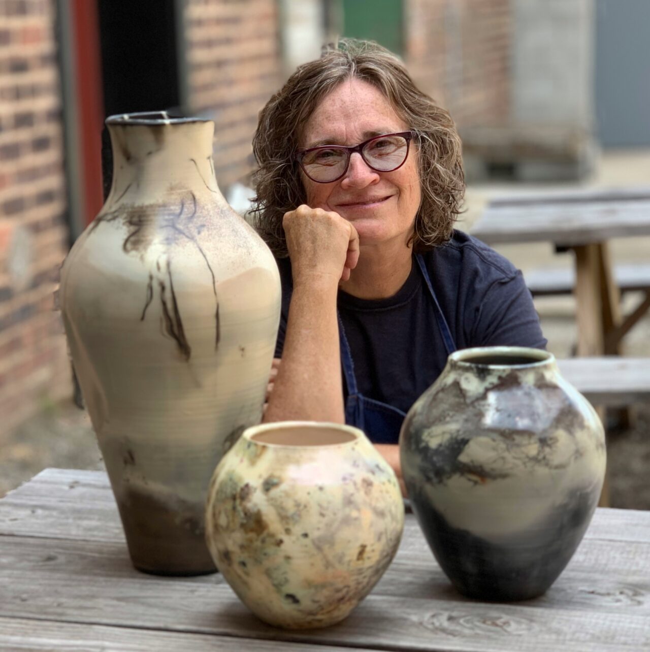 Judi Harwood sitting with a grouping of her finished pots, sagger pots