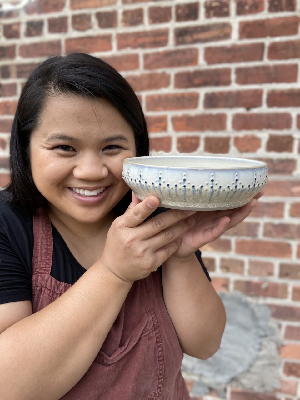 Katie Meili Messersmith holding finished pot close to face, dotted pasta bowl, dot pots