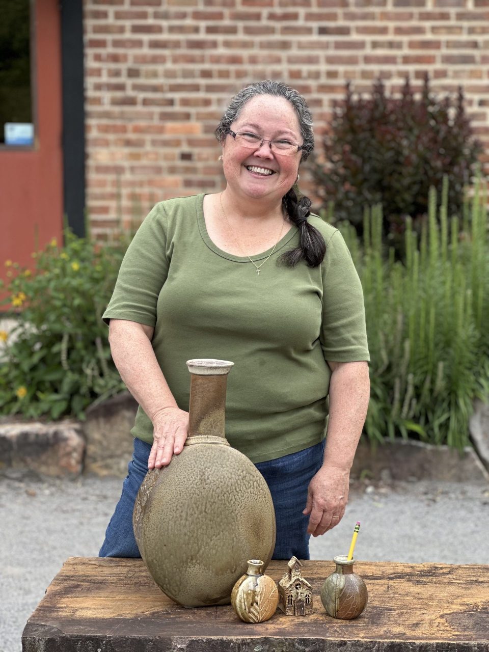 Karen Dubois standing with grouping of her finished pots, wood soda kazie pots, large vase