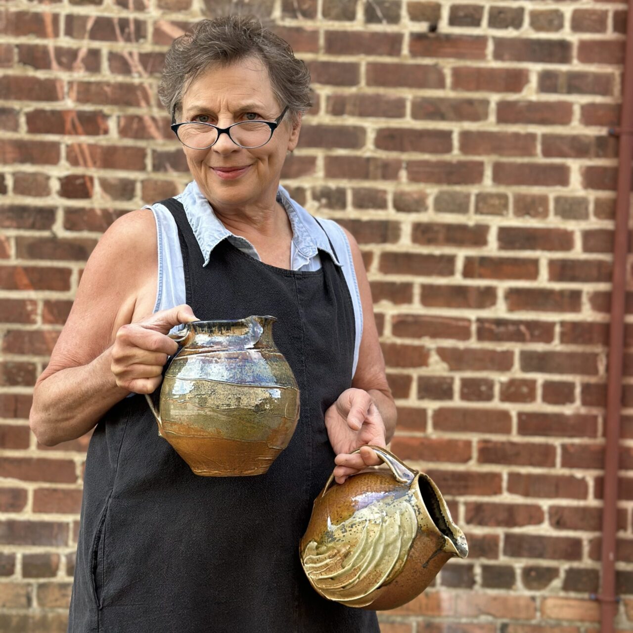 Sarah Wells Rolland holding two finished pots, wood soda kazie pitchers