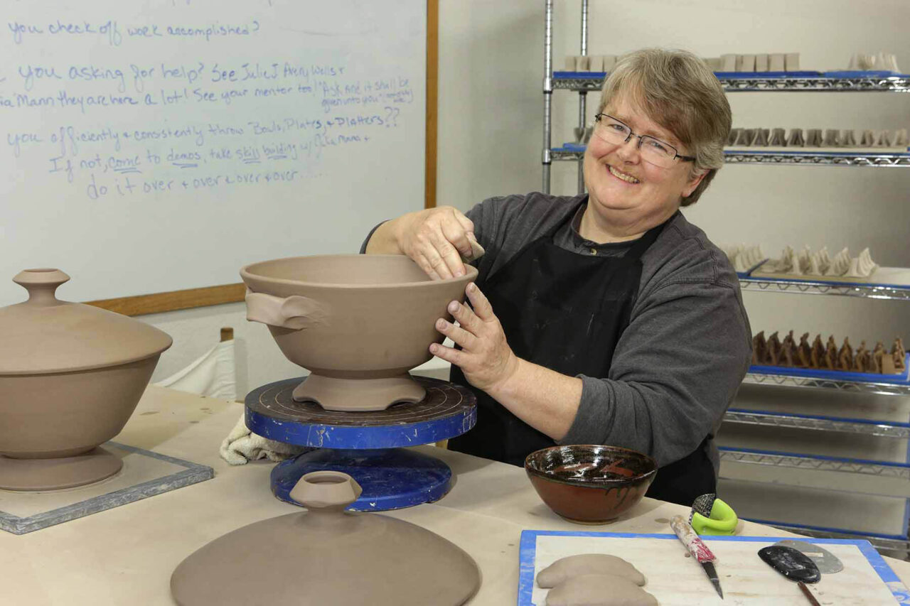 Julia Mann working on leather hard soup tureen, smiling