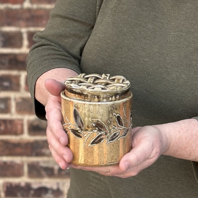 Karen Dubois holding finished hand built pot, vase with woven lid, wood soda kazie fired