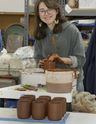 Avery Wells throwing red clay on the potters wheel in community ISM studio