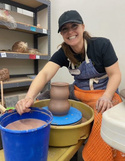 TVP Teaching Center Class student throwing at the wheel, Intermediate wheel Class, smiling with her vase