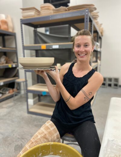 Teaching Center student showing fresh wheel thrown pot, sitting at wheel, intermediate wheel class