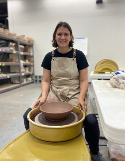 Teaching Center student smiling at potters wheel with fresh thrown bowl, intermediate wheel class