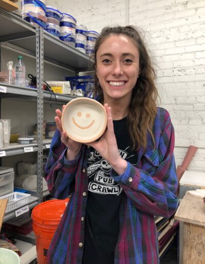 Teaching center student smiling with smiley face wax resist glazed pots, beginning wheel class