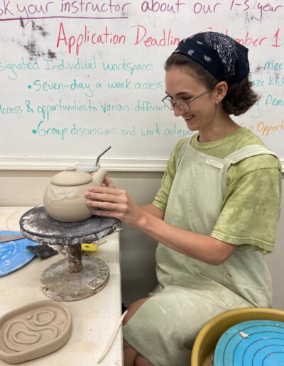 Teaching center student working on spout of leather hard teapot, happy, intermediate wheel class